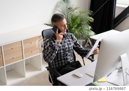 Businessman Talking on Phone and Reviewing Documents in Modern Office 116769867