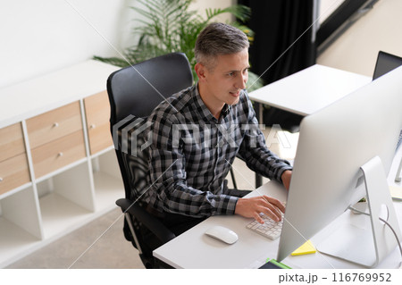 Focused Man Working on Computer in Modern Office Environment Focused Man Working on Computer in Modern Office Environment 116769952