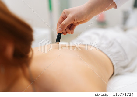 Closeup cropped shot of moxibustion treatment with smoke from moxa stick. Female client lying on spa bed during moxa smoke therapy. Spiritual healing, body and stress relief with Chinese treatment. 116771724