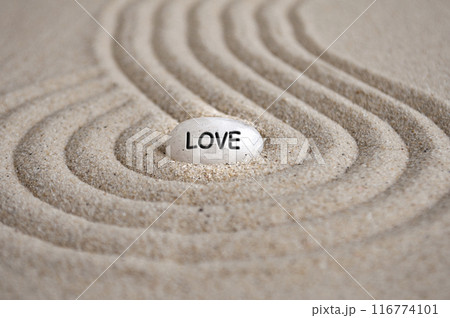 Love text engraved on Zen stone on sand with shining light. Love and romance concept 116774101