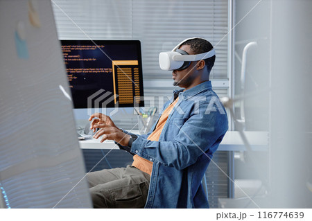 Side view shot of male African American software developer testing VR user experience wearing VR headset in IT company office, copy space 116774639