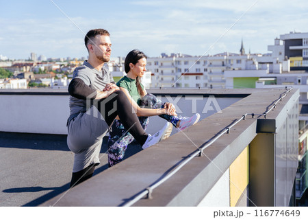Sportive Caucasian couple stretching together before doing exercise in urban area on rooftop. Warming up for workout outdoor in the morning. 116774649