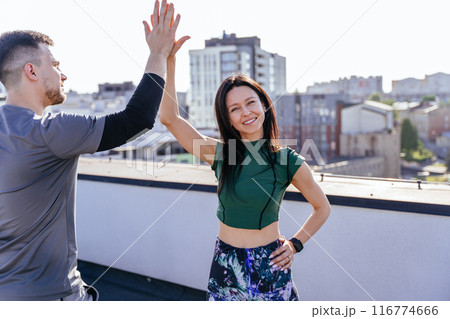 Handsome husband and wife enjoying end of physical morning warm-up. Two athletic people greeting each other with high five gesture during fit training on rooftop. 116774666
