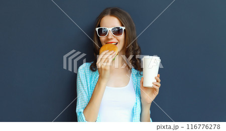 Happy cheerful young woman eating burger fast food holding cup of coffee, teenage girl having fun 116776278