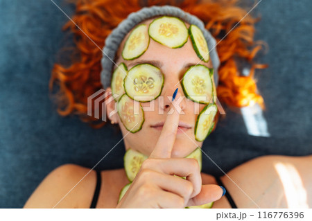 close-up face red-haired young woman with round slices of cucumber, cucumber mask on face 116776396