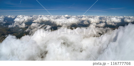 Aerial view from airplane window at high altitude of earth covered with white puffy cumulus clouds. 116777708