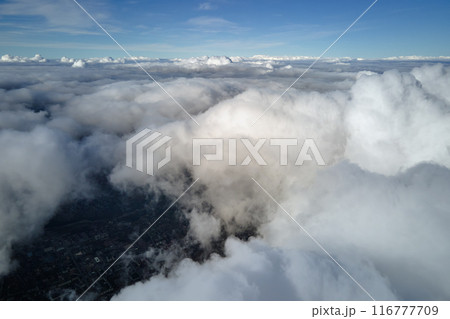 Aerial view from airplane window at high altitude of earth covered with puffy cumulus clouds forming before rainstorm 116777709