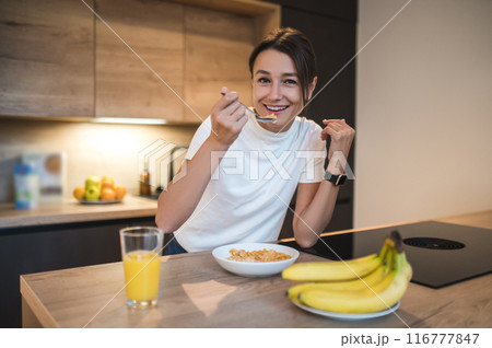 Dark-haired young woman having breakfast and looking contented Dark-haired young woman having breakfast and looking contented 116777847
