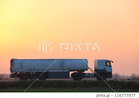 Semi-truck with tipping cargo trailer transporting sand from quarry driving on highway hauling goods in evening. Delivery transportation and logistics concept Semi-truck with tipping cargo trailer transporting sand from quarry driving on highway hauling goods in evening. Delivery transportation and logistics concept 116777977