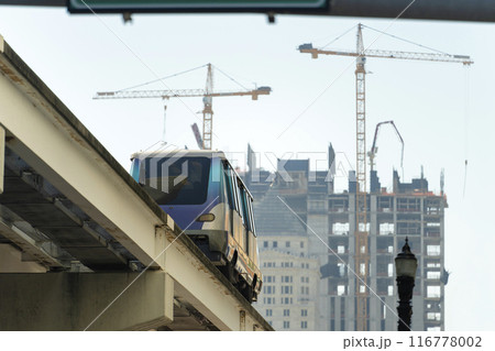 Public transportation in downtown Miami in Florida USA. Metrorail city train car on high railroad over street traffic between skyscraper buildings in modern American megapolis 116778002