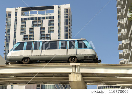 Public transportation in downtown Miami in Florida USA. Metrorail city train car on high railroad over street traffic between skyscraper buildings in modern American megapolis 116778003
