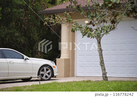 Vehicle parked in front of wide garage double door on paved driveway of typical contemporary american home 116778242