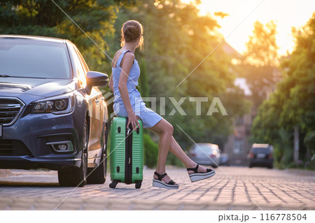 Young tired woman with suitcase sitting near her car waiting for someone. Travel and vacations concept. Young tired woman with suitcase sitting near her car waiting for someone. Travel and vacations concept. 116778504
