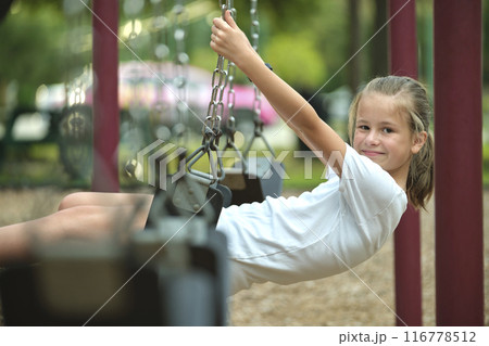 Young pretty smiling teenage girl playing alone on swings on summer playground Young pretty smiling teenage girl playing alone on swings on summer playground 116778512
