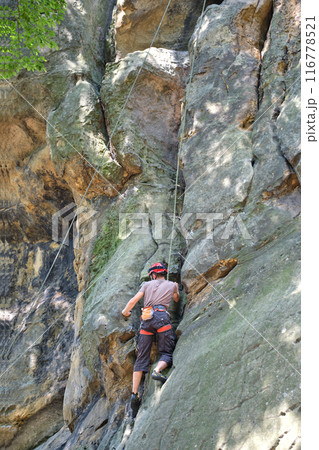 Young man climbing steep wall of rocky mountain. Male climber overcomes challenging route. Engaging in extreme sport concept. Young man climbing steep wall of rocky mountain. Male climber overcomes challenging route. Engaging in extreme sport concept. 116778521