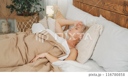 Leisure morning. Sleeping resting. Wonderful rest. Relaxed woman covered with blanket enjoying free time laying in comfortable bed in light home interior. 116780858