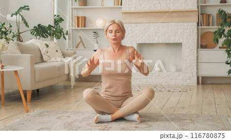 Breathing practice. Healing exercise. Peaceful calm woman sitting in yoga pose on floor inhaling exhaling deeply in living room home interior. 116780875