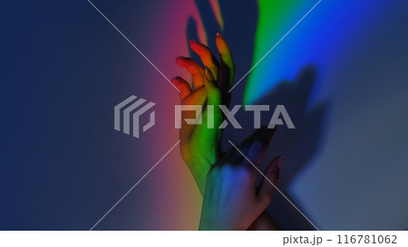 Rainbow touch. LGBT spectrum. Gay pride. Color inspiration. Tender female hands gesture in blur bright neon light gradient on free space blue shadow background. 116781062