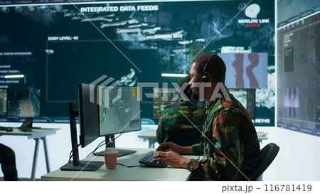 Army intelligence specialist utilize advanced computer systems, surveillance technology and data to enhance national security. Working in a command post against potential threats. Camera B. 116781419