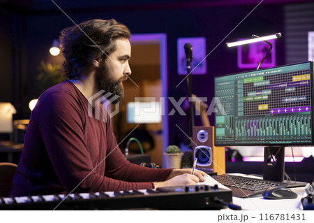 Songwriter taking notes to create new music in his home studio, writing down lyrics and harmonic elements before recording his song on daw software, acoustical engineering post production. Songwriter taking notes to create new music in his home studio, writing down lyrics and harmonic elements before recording his song on daw software, acoustical engineering post production. 116781431