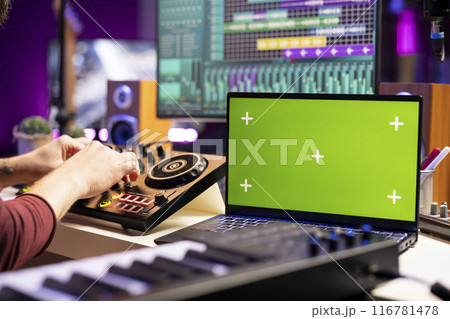 Sound engineer twisting pre amp knobs on mixing console in home studio, using laptop with greenscreen template. Music producer editing soundtracks, stereo equipment on daw software. 116781478