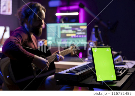 Singer producer playing acoustic guitar looking at daw software interface to record new tunes, learning accords on instrument strings. Composer singing songs next to greenscreen on tablet. Singer producer playing acoustic guitar looking at daw software interface to record new tunes, learning accords on instrument strings. Composer singing songs next to greenscreen on tablet. 116781485