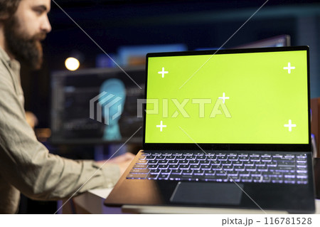 Focus on green screen laptop used by engineer wearing EEG headset in blurry background to upload consciousness into computer. Close up of mockup laptop used by IT expert to create upload brain Focus on green screen laptop used by engineer wearing EEG headset in blurry background to upload consciousness into computer. Close up of mockup laptop used by IT expert to create upload brain 116781528
