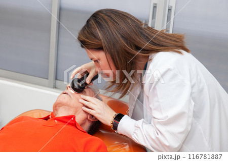 Dermatologist  making a routine checkup on a senior male patient using a magnifying glass. 116781887