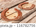 Two old vintage and rusty horseshoes are nailed to a dried and cracked piece of wood. 116782756
