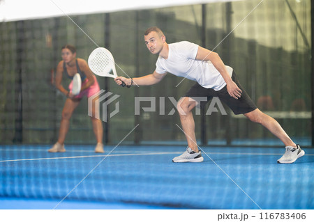 Male players playing padel in a padel court indoor behind net 116783406
