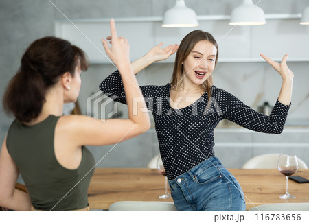 At home two women dance with glass of wine in their hands in kitchen 116783656