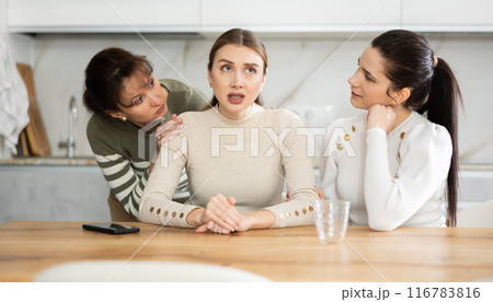 Sad middle-aged woman sitting at table while two others trying to calm her 116783816