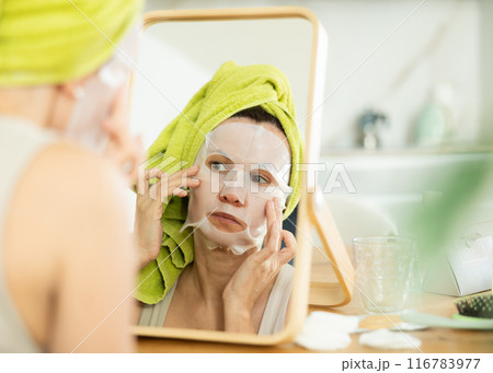 Woman with towel head wrap applying cosmetic face mask Woman with towel head wrap applying cosmetic face mask 116783977
