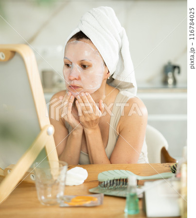Woman with towel head wrap applying cosmetic face mask Woman with towel head wrap applying cosmetic face mask 116784025