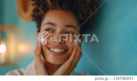 Beautiful mixed race woman with short curly hair applying facial cream and smiling 116786843