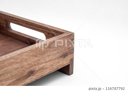 Solid walnut wood tray with dovetail joints and cutout handles on the sides for easy carrying closeup view on white background Solid walnut wood tray with dovetail joints and cutout handles on the sides for easy carrying closeup view on white background 116787792
