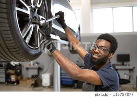 Smiling mechanic repairing car wheel in modern garage 116787877