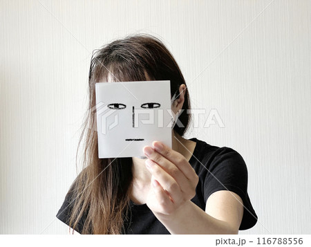 顔の前で見つめる顔イラストの紙を片手で持つ女性 116788556