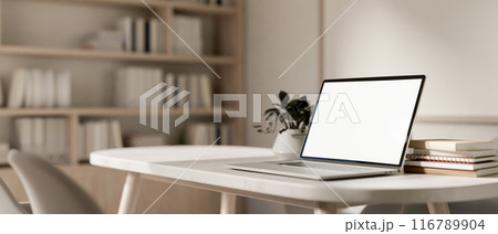A close-up image of a laptop computer with a white-screen mockup on a table in a contemporary room. 116789904
