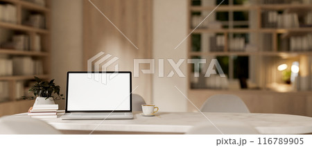A laptop computer with a white-screen mockup on a white marble table in a contemporary cozy room. 116789905