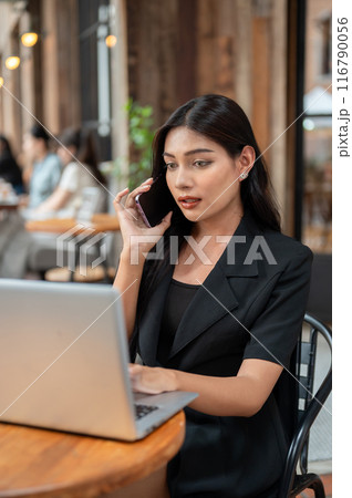 A confident Asian businesswoman is talking on the phone while working on her laptop at a cafe. A confident Asian businesswoman is talking on the phone while working on her laptop at a cafe. 116790056