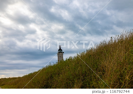 A picturesque lighthouse on a grassy hill with a dramatic sky creates a stunning coastal view A picturesque lighthouse on a grassy hill with a dramatic sky creates a stunning coastal view 116792744