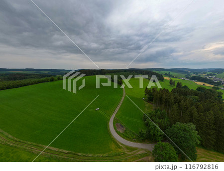 Aerial view of green countryside with winding road under cloudy sky looks picturesque and tranquil 116792816
