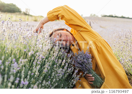 woman in a yellow dress leans into blooming lavender flowers, holding a bouquet, embracing the natural beauty around her. 116793497