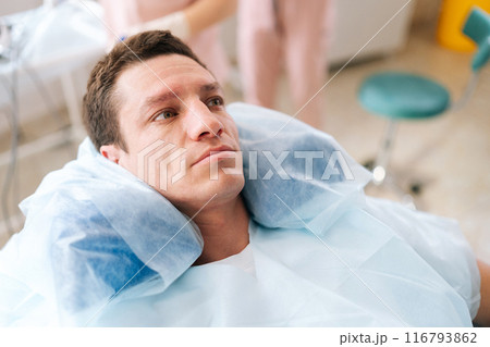Close-up portrait of cosmetology male client pensive looking away lying on medical chair modern clinic. Handsome young man waiting for dermatologist cosmetologist consultation in beauty salon. Close-up portrait of cosmetology male client pensive looking away lying on medical chair modern clinic. Handsome young man waiting for dermatologist cosmetologist consultation in beauty salon. 116793862