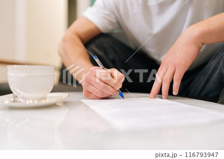Closeup hands of unrecognizable male client signing papers sitting at table in waiting room. Young man with pen putting signature on medical card official contract agreement, writing documents. Closeup hands of unrecognizable male client signing papers sitting at table in waiting room. Young man with pen putting signature on medical card official contract agreement, writing documents. 116793947