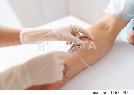 Closeup of preparation for blood test with male patient by female doctor in gloves on table in white bright room. Nurse pierces man patient arm vein with needle tube. Concept of medical treatment Closeup of preparation for blood test with male patient by female doctor in gloves on table in white bright room. Nurse pierces man patient arm vein with needle tube. Concept of medical treatment 116793975