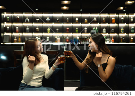 Attractive female friends toasting with drinks in the bar. Nightlife, celebrations and friendship concept 116794261