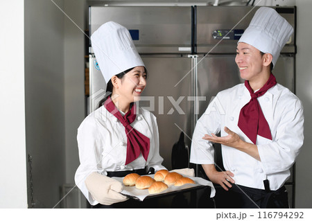 ベーカリーの厨房で会話するパン職人の男女 116794292