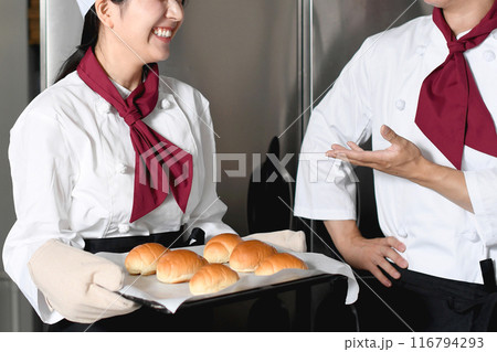 ベーカリーの厨房で会話するパン職人の男女 116794293